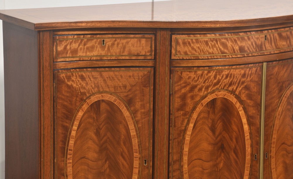 A Sheraton Revival bow-front wooden sideboard featuring oval inlaid veneer door panels, top drawers, and square tapered legs. View V