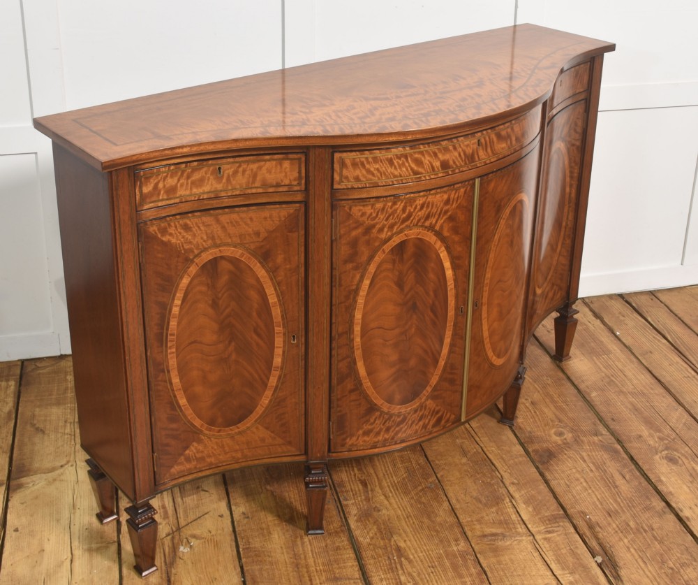 A Sheraton Revival bow-front wooden sideboard featuring oval inlaid veneer door panels, top drawers, and square tapered legs. View VI