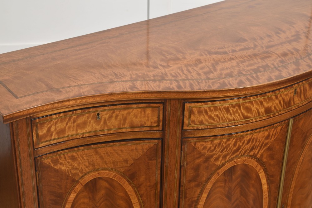 A Sheraton Revival bow-front wooden sideboard featuring oval inlaid veneer door panels, top drawers, and square tapered legs. View VII