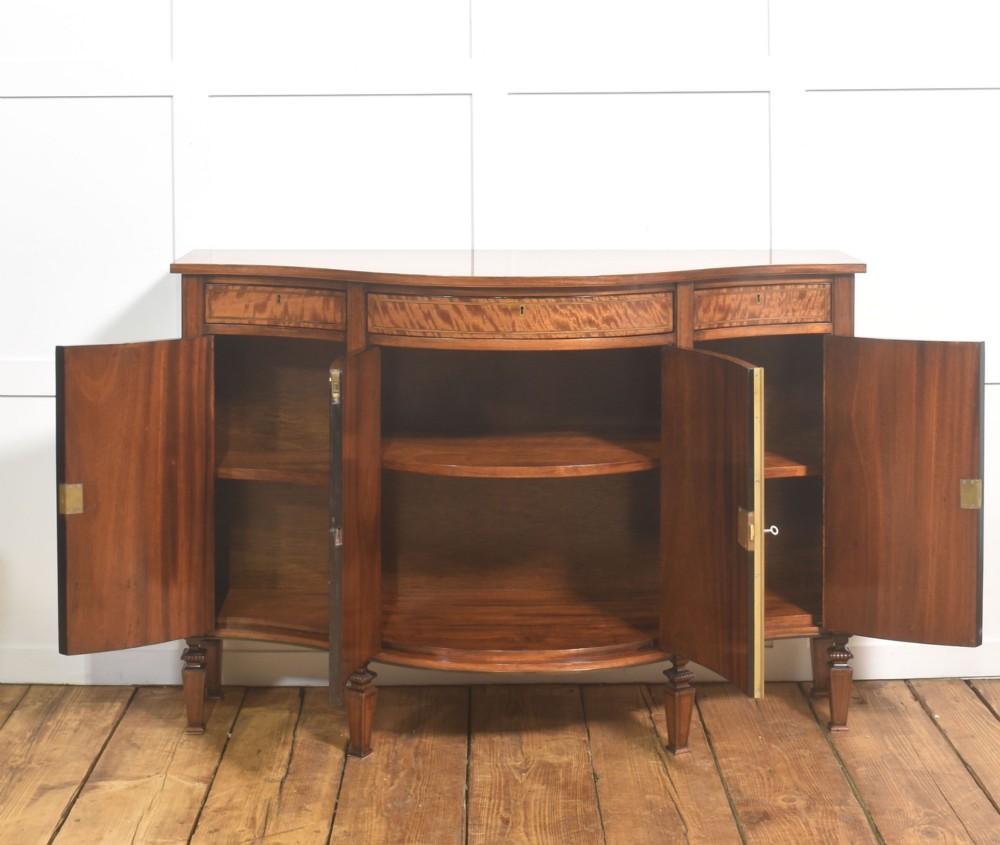 A Sheraton Revival bow-front wooden sideboard featuring oval inlaid veneer door panels, top drawers, and square tapered legs. View VIII