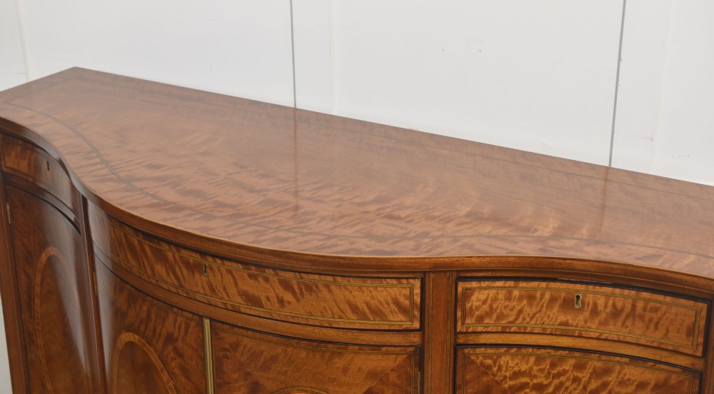 A Sheraton Revival bow-front wooden sideboard featuring oval inlaid veneer door panels, top drawers, and square tapered legs. View XI