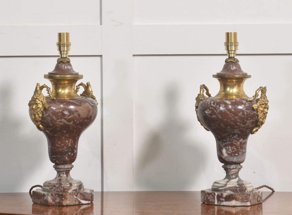A pair of urn-shaped table lamps crafted from veined red marble with gilt brass collars and decorative side handles.