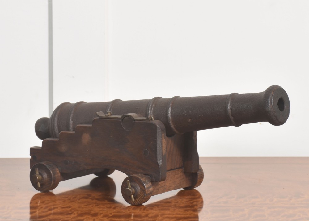 A 19th-century cast iron signal cannon mounted on a stepped dark oak carriage with wooden wheels.