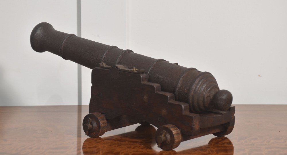 A 19th-century cast iron signal cannon mounted on a stepped dark oak carriage with wooden wheels. View IV