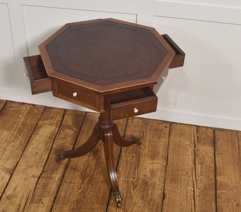 A Regency Revival mahogany octagonal drum table featuring an inset dark leather top, apron drawers, and a central turned pedestal with tripod reeded legs resting on brass castors. View V