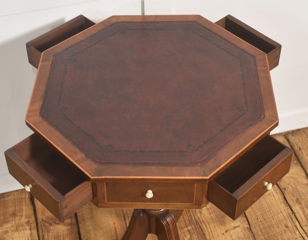 A Regency Revival mahogany octagonal drum table featuring an inset dark leather top, apron drawers, and a central turned pedestal with tripod reeded legs resting on brass castors. View VII