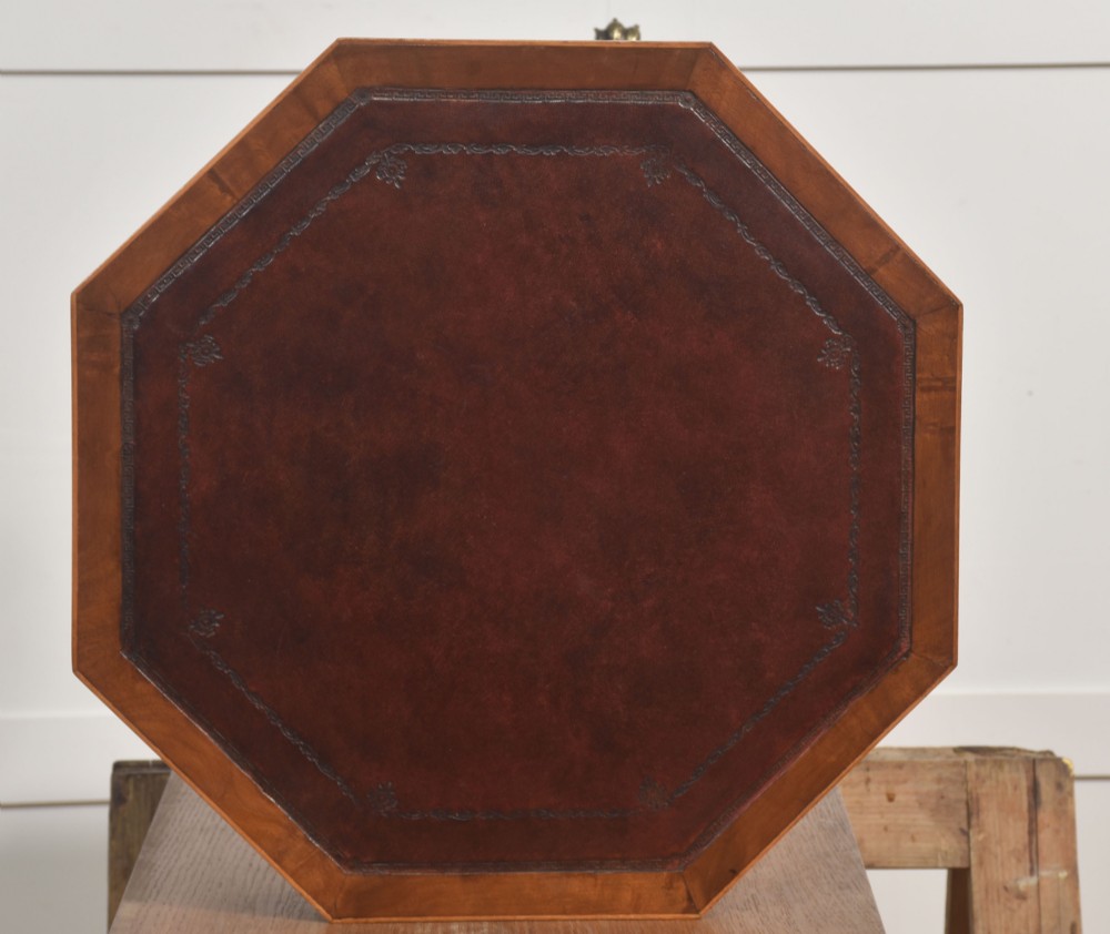 A Regency Revival mahogany octagonal drum table featuring an inset dark leather top, apron drawers, and a central turned pedestal with tripod reeded legs resting on brass castors. View VIII