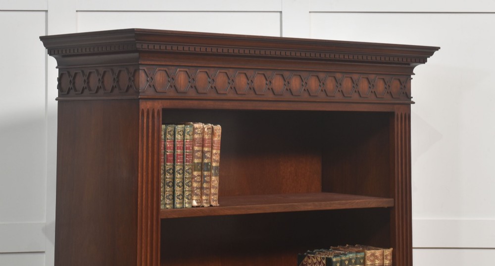 A tall mahogany open bookcase featuring adjustable shelves, fluted side pilasters, and a carved geometric frieze beneath a moulded cornice. View V