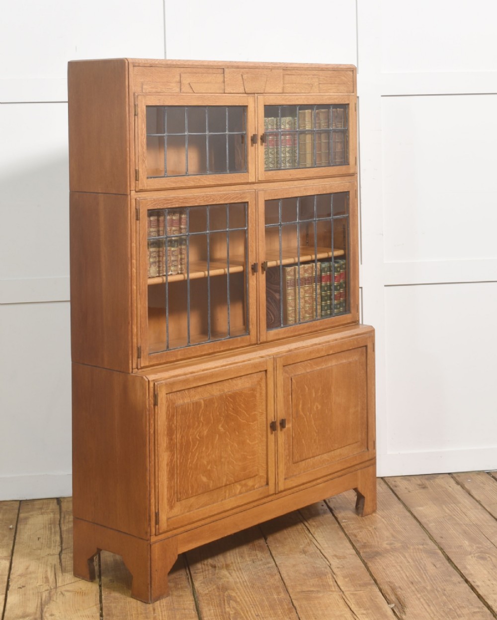 An Art Deco medium oak bookcase featuring two upper sections with leaded glass doors above a double-door base cupboard. View IV