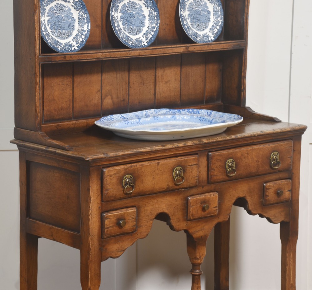 An antique warm brown oak dresser featuring an upper three-shelf plate rack with a scalloped canopy, sitting above five drawers and an open pot shelf with a turned central support. View VI