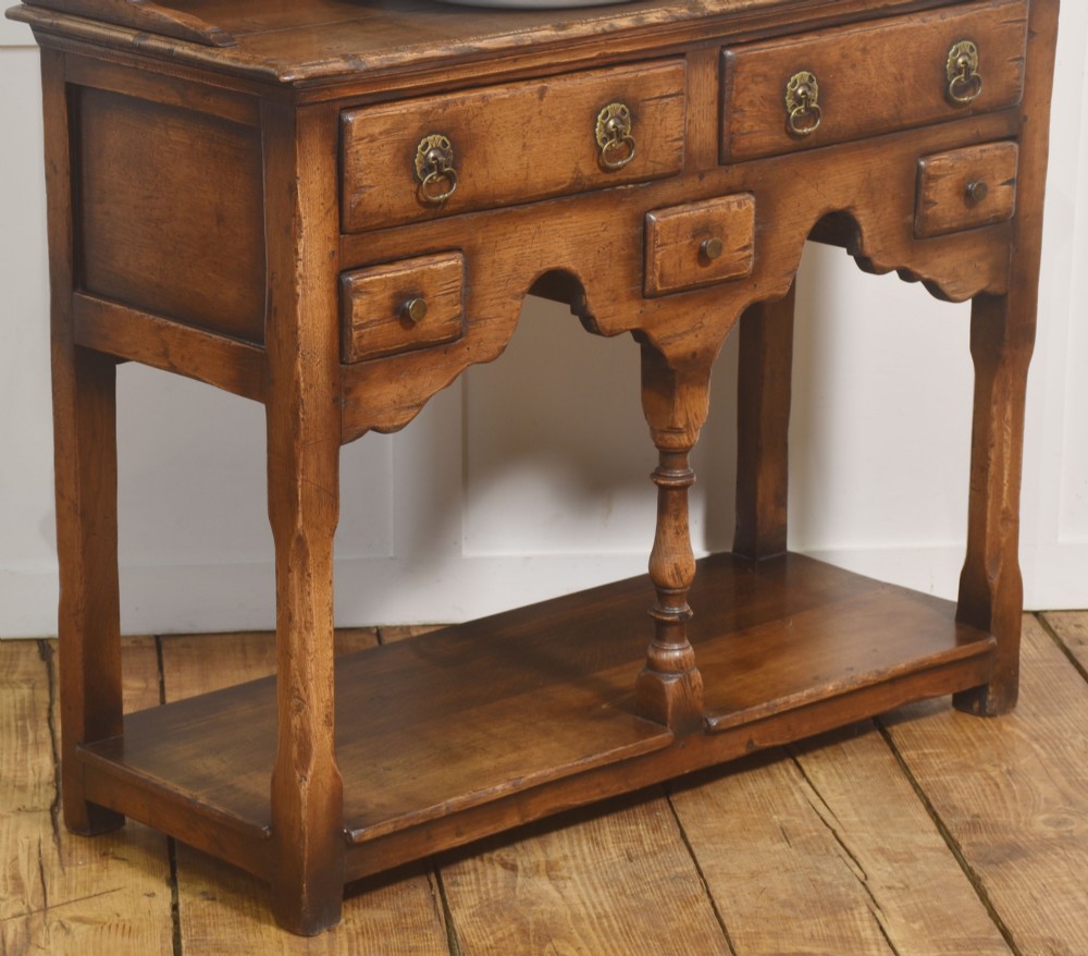 An antique warm brown oak dresser featuring an upper three-shelf plate rack with a scalloped canopy, sitting above five drawers and an open pot shelf with a turned central support. View VII