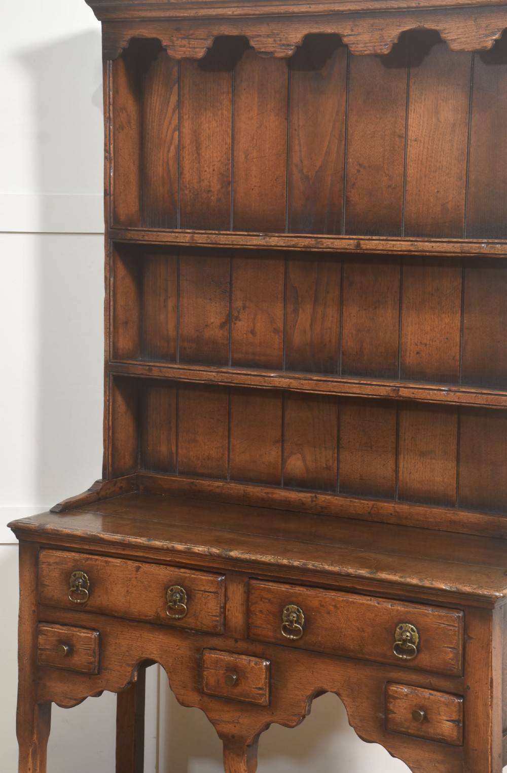 An antique warm brown oak dresser featuring an upper three-shelf plate rack with a scalloped canopy, sitting above five drawers and an open pot shelf with a turned central support. View IX
