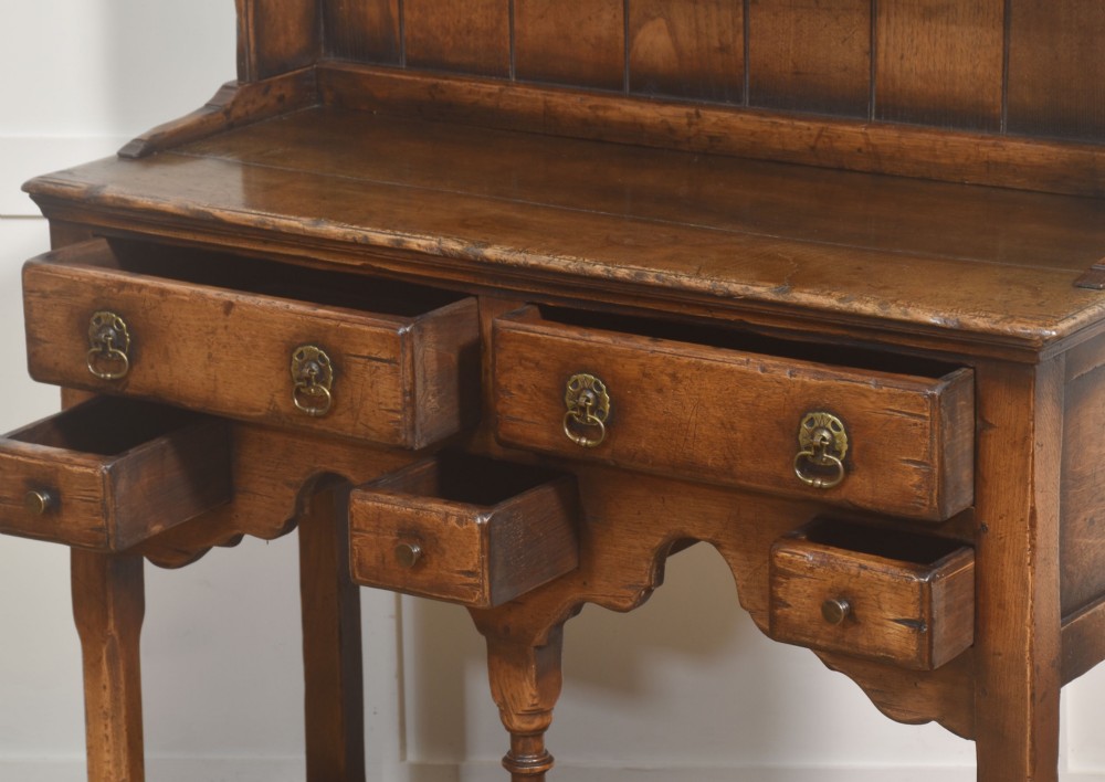 An antique warm brown oak dresser featuring an upper three-shelf plate rack with a scalloped canopy, sitting above five drawers and an open pot shelf with a turned central support. View XI