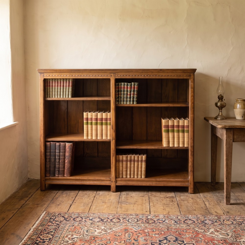 A low freestanding solid oak open bookcase featuring a double bay configuration, carved frieze detail, and adjustable shelves housing books. View II