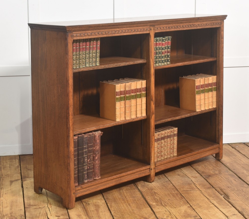A low freestanding solid oak open bookcase featuring a double bay configuration, carved frieze detail, and adjustable shelves housing books. View III