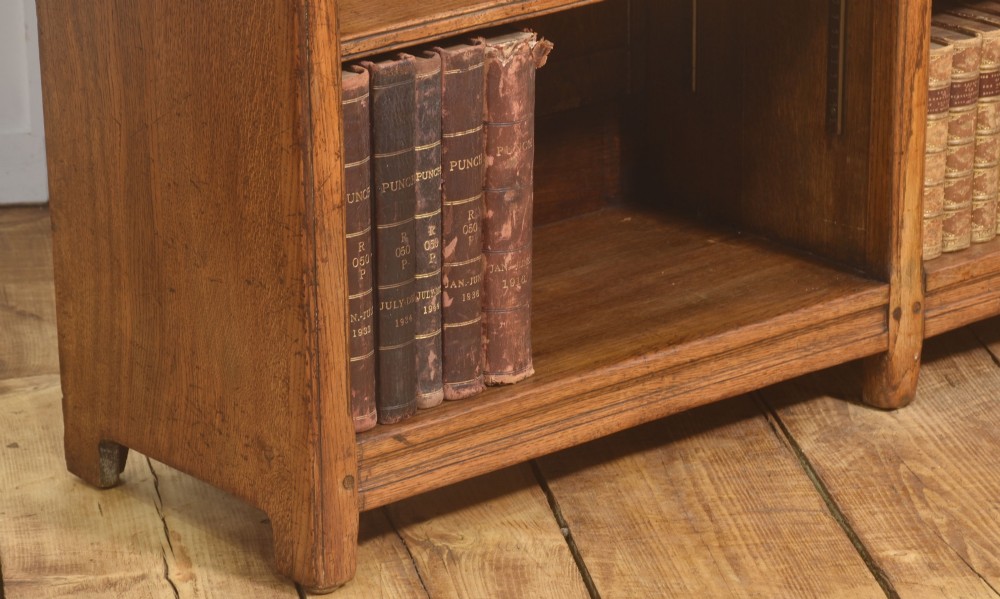A low freestanding solid oak open bookcase featuring a double bay configuration, carved frieze detail, and adjustable shelves housing books. View IV