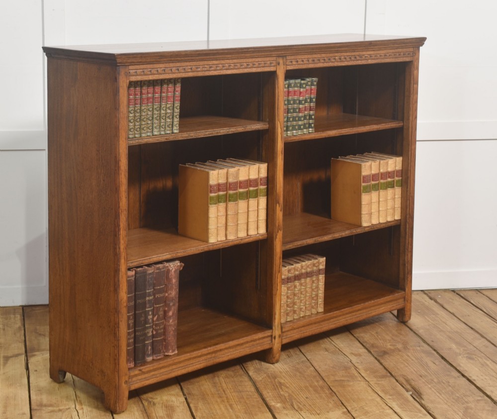 A low freestanding solid oak open bookcase featuring a double bay configuration, carved frieze detail, and adjustable shelves housing books. View V