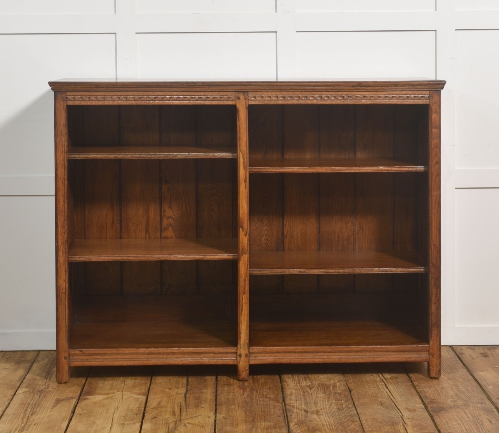 A low freestanding solid oak open bookcase featuring a double bay configuration, carved frieze detail, and adjustable shelves housing books. View VIII