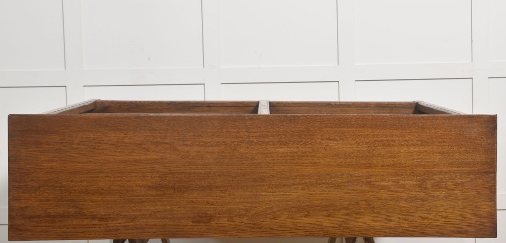 A low freestanding solid oak open bookcase featuring a double bay configuration, carved frieze detail, and adjustable shelves housing books. View XI