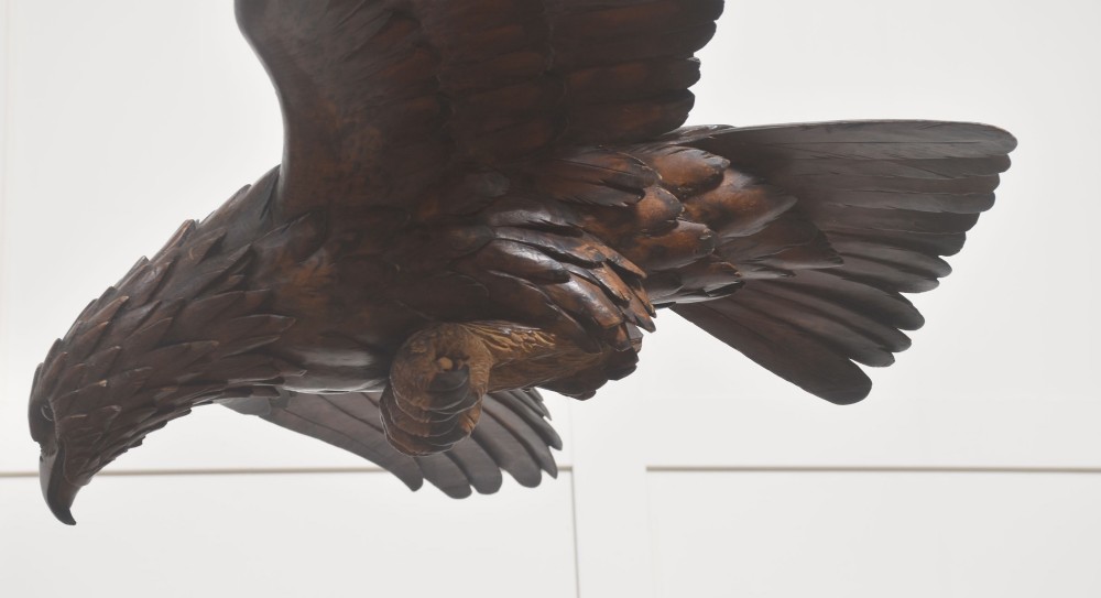 A dark wood eagle sculpture hand-carved in mid-flight with outstretched wings and carved feather detailing. View VII