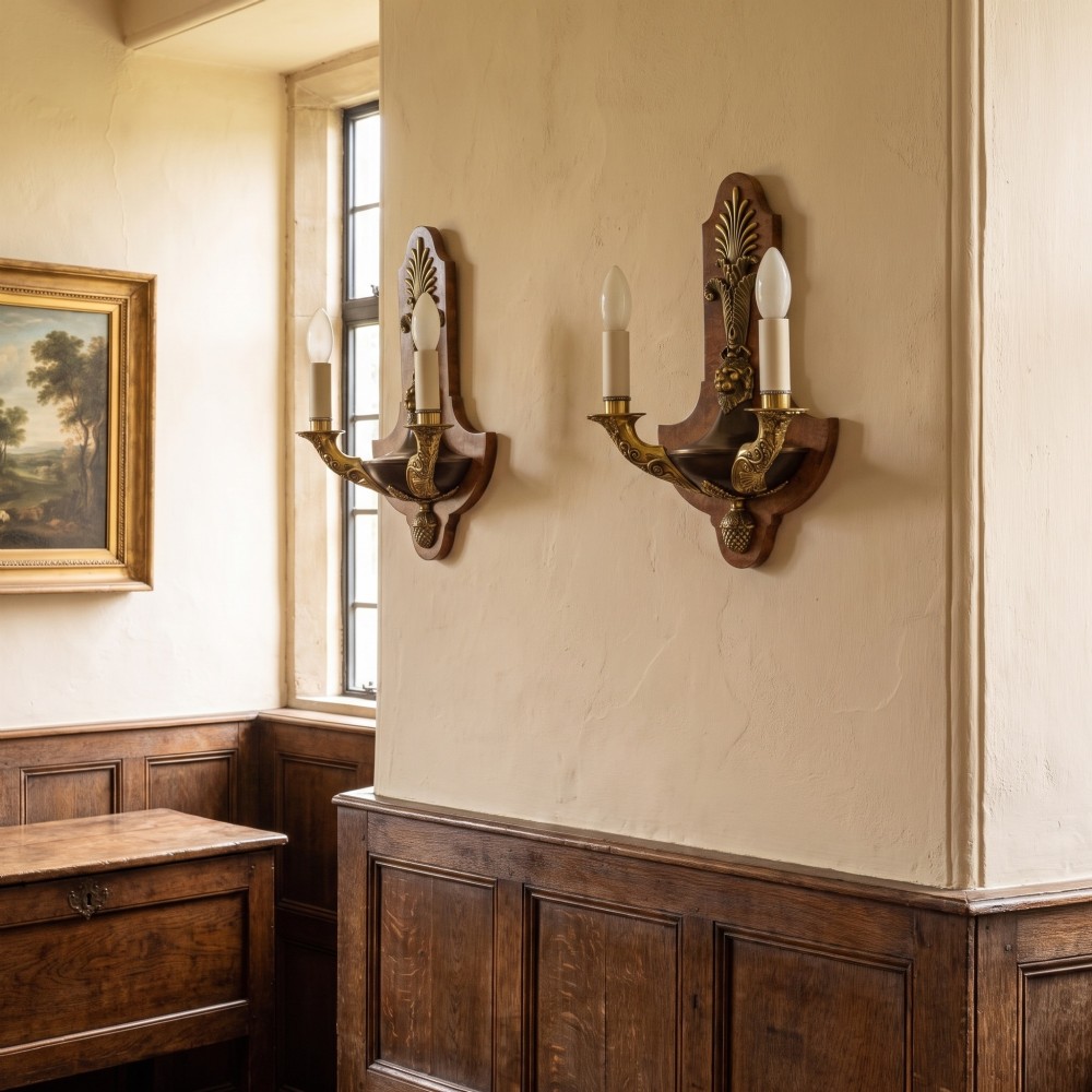 A pair of Empire style wall lights featuring shaped burr walnut backplates decorated with brass lion masks, anthemion crests, and twin scrolling candle arms. View II