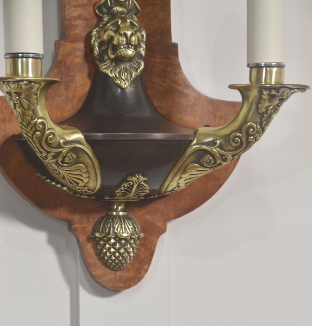 A pair of Empire style wall lights featuring shaped burr walnut backplates decorated with brass lion masks, anthemion crests, and twin scrolling candle arms. View V