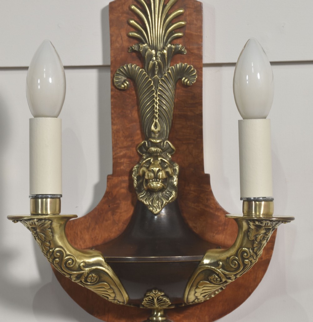 A pair of Empire style wall lights featuring shaped burr walnut backplates decorated with brass lion masks, anthemion crests, and twin scrolling candle arms. View VI