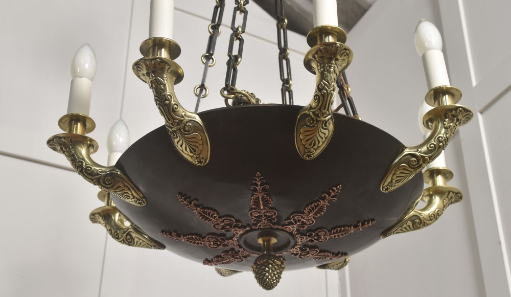 An Empire Revival brass and copper eight-light chandelier featuring a central dish supported by link chains and decorated with cast brass mounts and candle-style lights. View IV