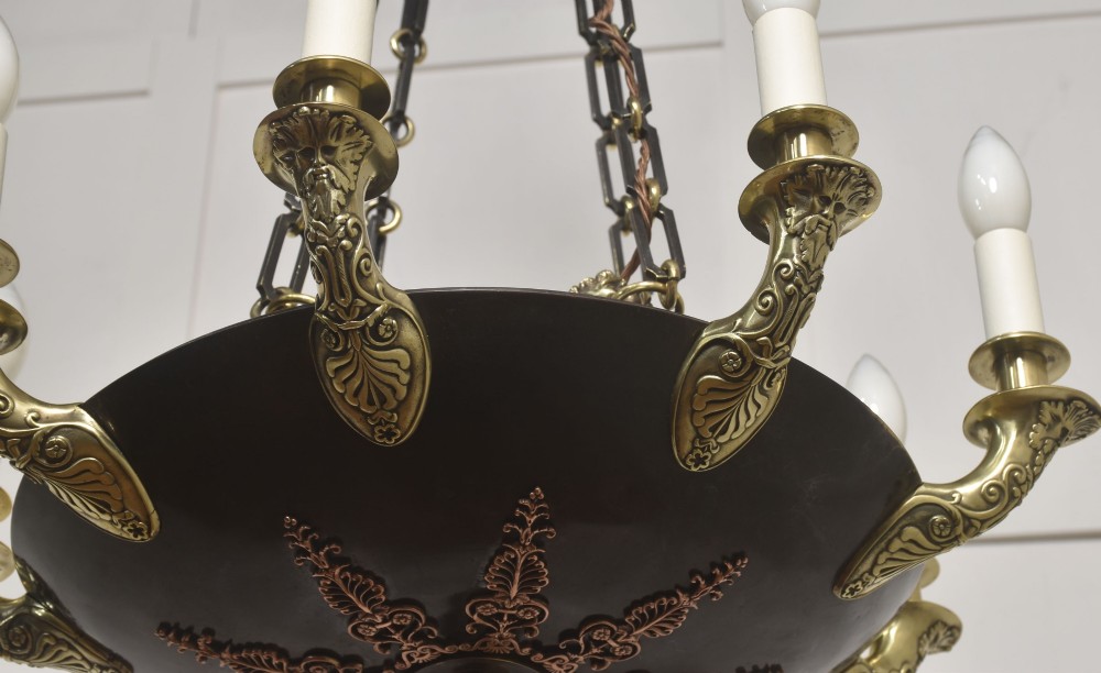 An Empire Revival brass and copper eight-light chandelier featuring a central dish supported by link chains and decorated with cast brass mounts and candle-style lights. View V