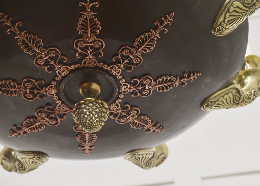 An Empire Revival brass and copper eight-light chandelier featuring a central dish supported by link chains and decorated with cast brass mounts and candle-style lights. View VIII