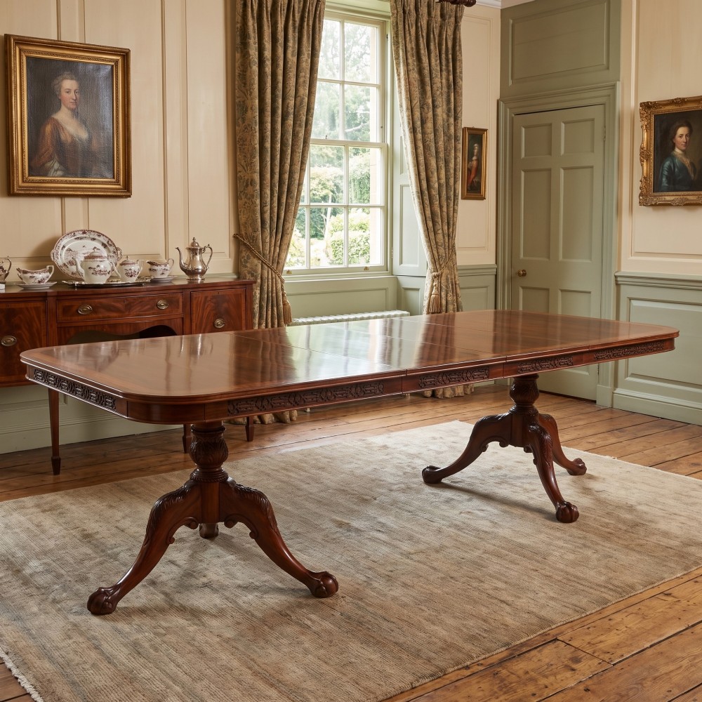 A large Chippendale revival mahogany extending dining table with a crossbanded top, carved frieze, and twin pedestal bases terminating in ball and claw feet. View II