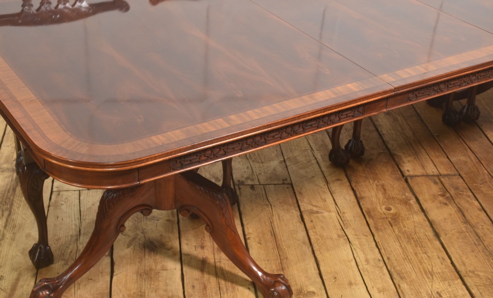 A large Chippendale revival mahogany extending dining table with a crossbanded top, carved frieze, and twin pedestal bases terminating in ball and claw feet. View IV
