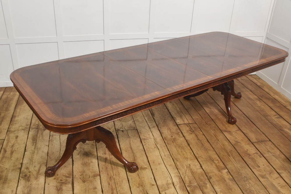 A large Chippendale revival mahogany extending dining table with a crossbanded top, carved frieze, and twin pedestal bases terminating in ball and claw feet.