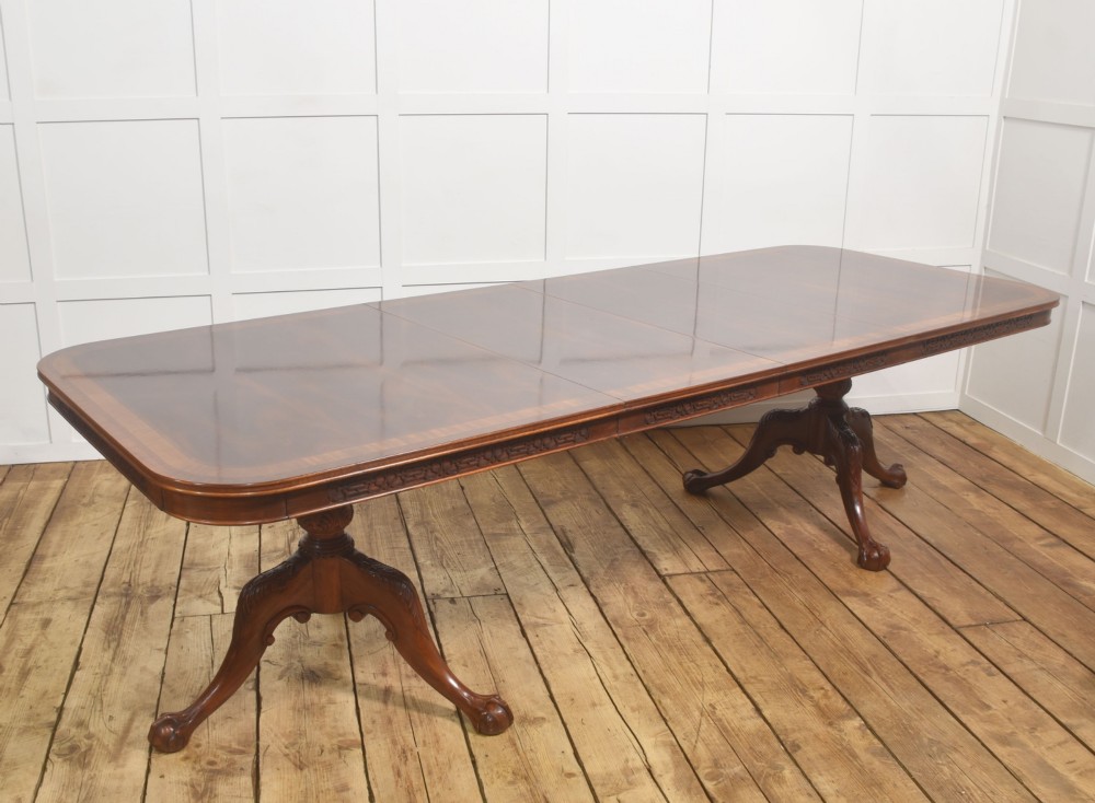 A large Chippendale revival mahogany extending dining table with a crossbanded top, carved frieze, and twin pedestal bases terminating in ball and claw feet. View V