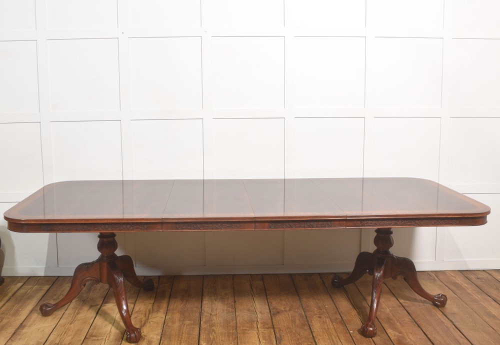 A large Chippendale revival mahogany extending dining table with a crossbanded top, carved frieze, and twin pedestal bases terminating in ball and claw feet. View VI