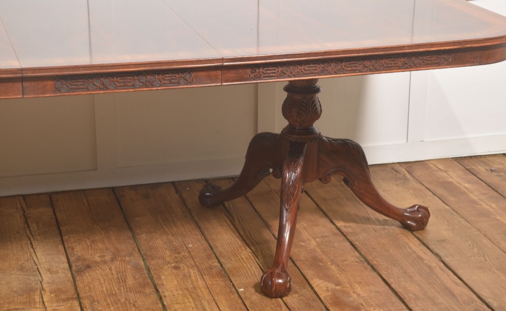 A large Chippendale revival mahogany extending dining table with a crossbanded top, carved frieze, and twin pedestal bases terminating in ball and claw feet. View VII