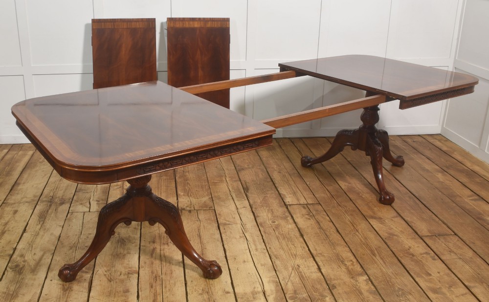 A large Chippendale revival mahogany extending dining table with a crossbanded top, carved frieze, and twin pedestal bases terminating in ball and claw feet. View IX