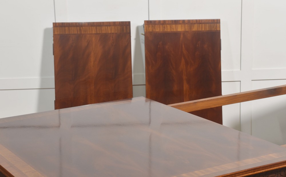 A large Chippendale revival mahogany extending dining table with a crossbanded top, carved frieze, and twin pedestal bases terminating in ball and claw feet. View X