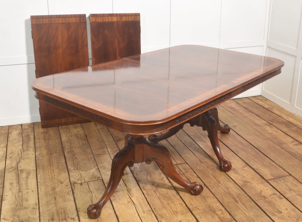 A large Chippendale revival mahogany extending dining table with a crossbanded top, carved frieze, and twin pedestal bases terminating in ball and claw feet. View XI
