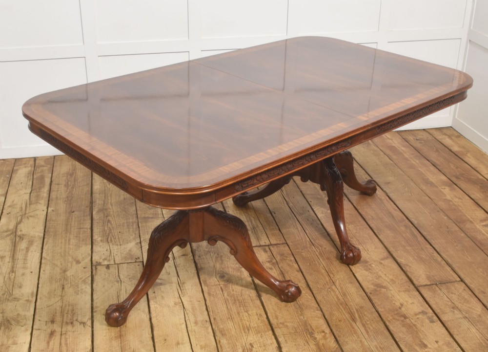 A large Chippendale revival mahogany extending dining table with a crossbanded top, carved frieze, and twin pedestal bases terminating in ball and claw feet. View XII