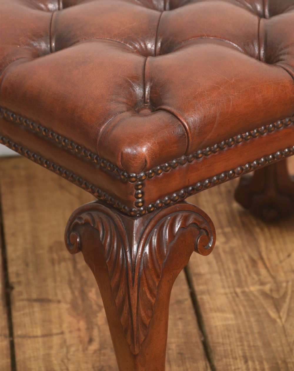 A deep-buttoned brown leather stool featuring brass stud detailing and carved mahogany cabriole legs ending in ball-and-claw feet. View V