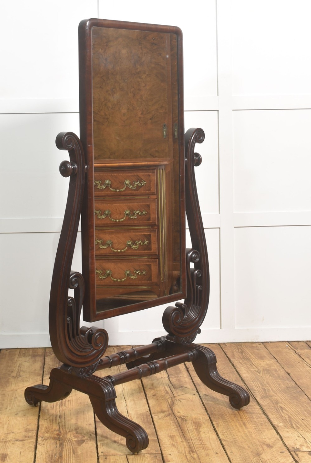 A William IV mahogany cheval mirror featuring carved scroll upright supports, a tilting full-length rectangular glass frame, and a stretcher base with swept feet.