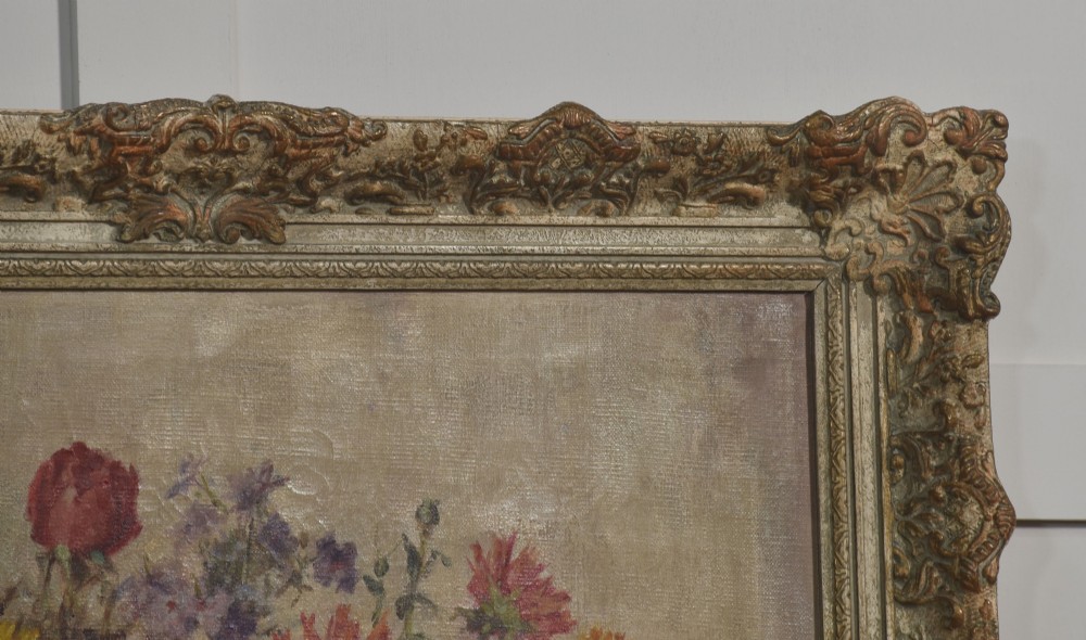 An oil painting on canvas depicting a colourful floral arrangement in a silver urn vase, set within a heavily carved gilt frame. View V