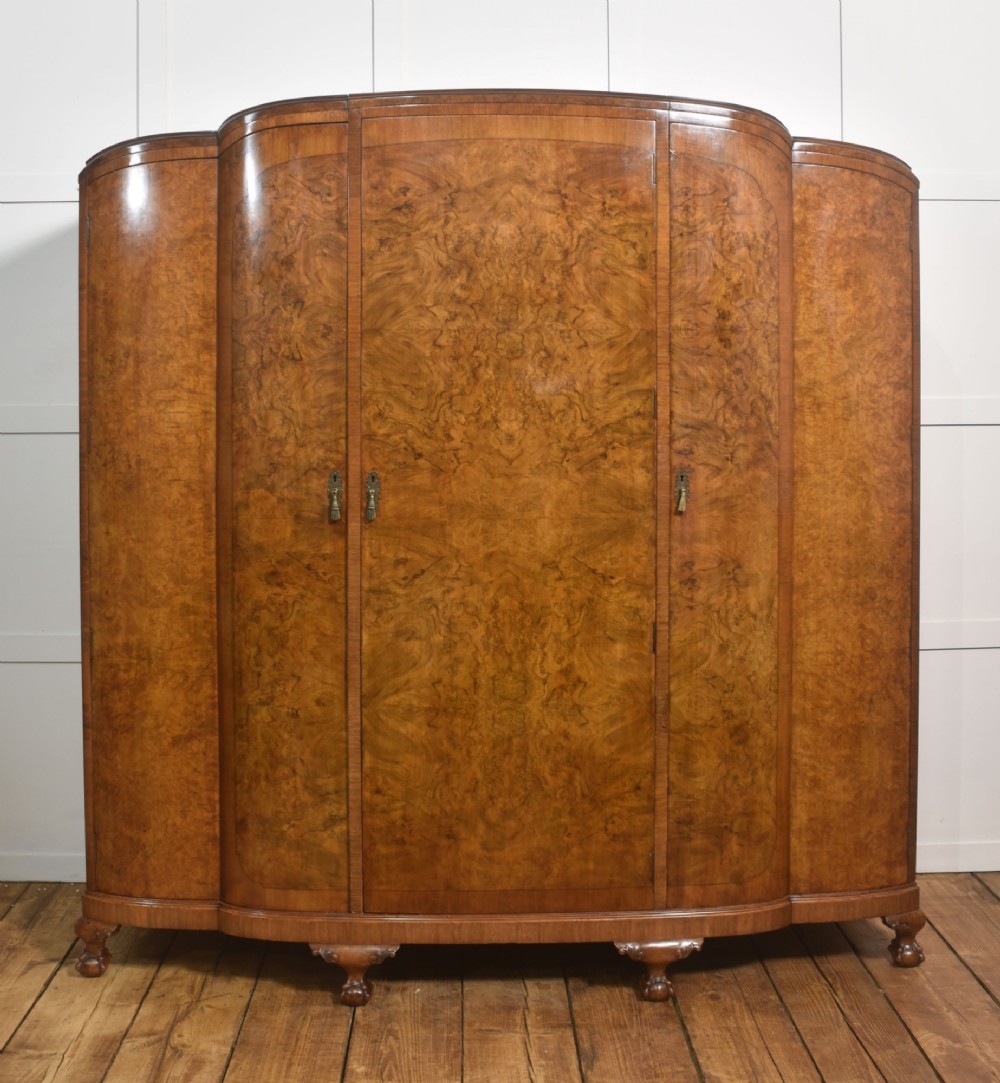 An Art Deco burr walnut breakfront wardrobe with curved side doors, a raised central door, and short carved feet.
