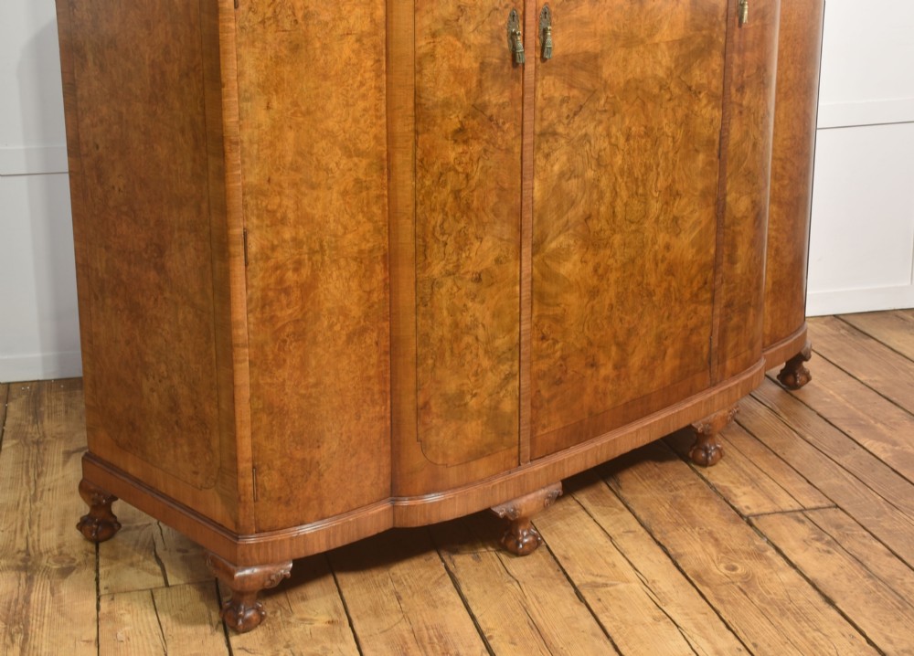 An Art Deco burr walnut breakfront wardrobe with curved side doors, a raised central door, and short carved feet. View IX
