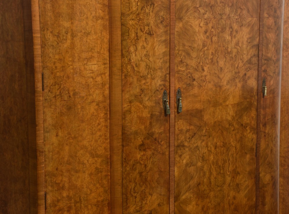 An Art Deco burr walnut breakfront wardrobe with curved side doors, a raised central door, and short carved feet. View X