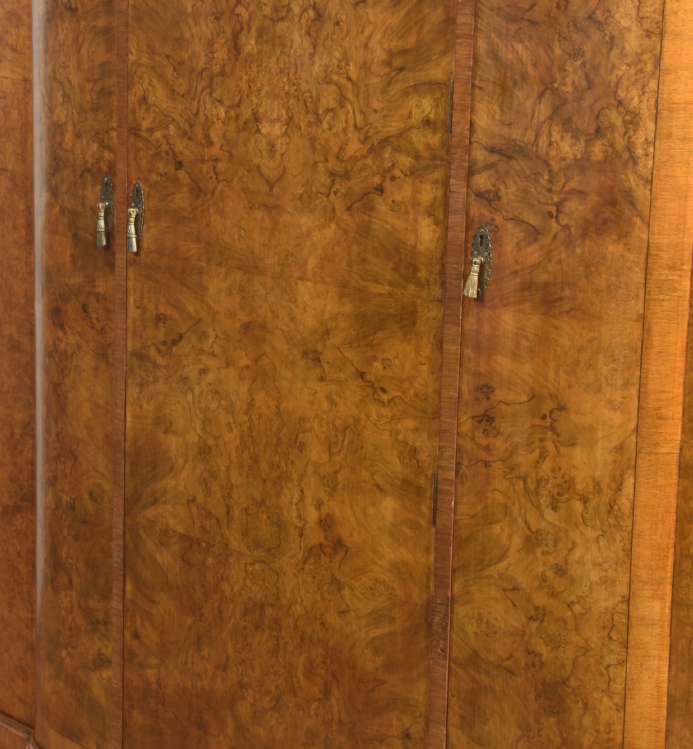 An Art Deco burr walnut breakfront wardrobe with curved side doors, a raised central door, and short carved feet. View XII