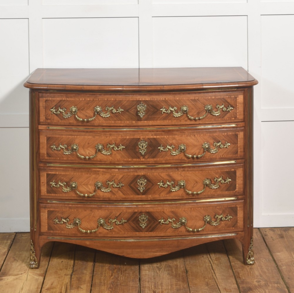A French Louis XV style serpentine chest of drawers featuring geometric wood marquetry and decorative brass handles.