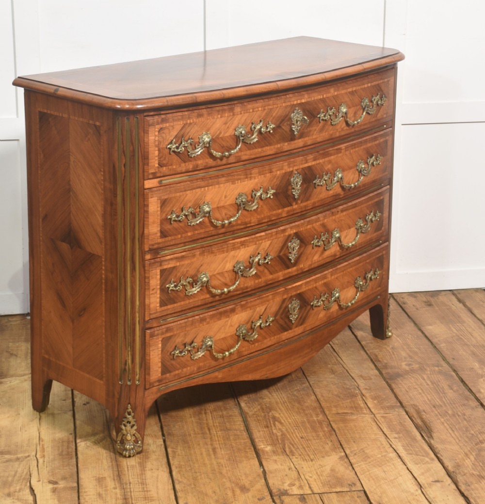 A French Louis XV style serpentine chest of drawers featuring geometric wood marquetry and decorative brass handles. View III