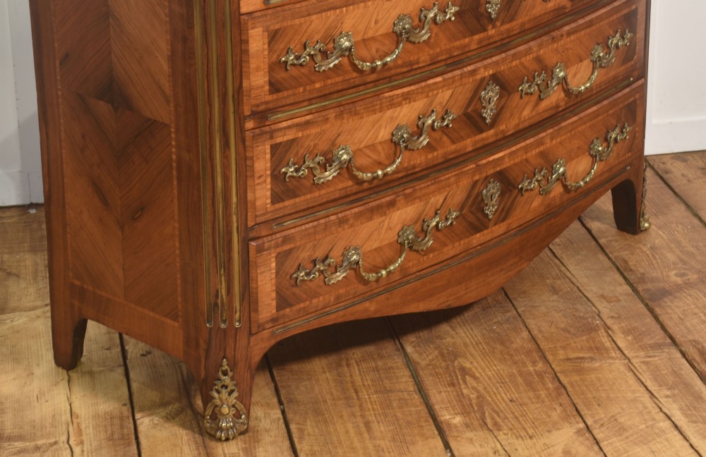 A French Louis XV style serpentine chest of drawers featuring geometric wood marquetry and decorative brass handles. View IV